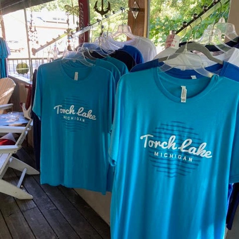 Blue Torch Lake Michigan T-shirts hanging on a rack in a shop.