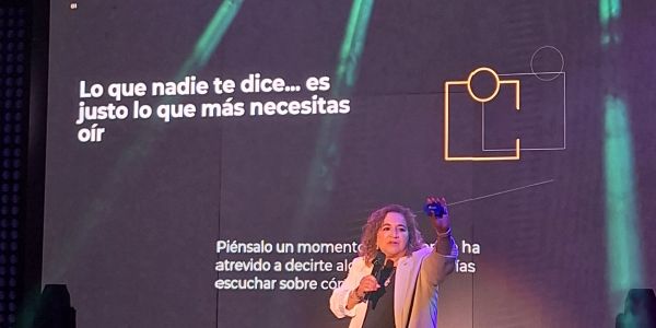 A speaker presents on stage with an inspiring Spanish quote in the background.