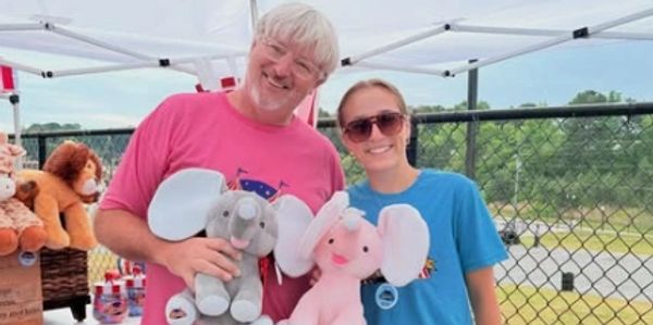 Two people holding elephant plush toys and smiling.