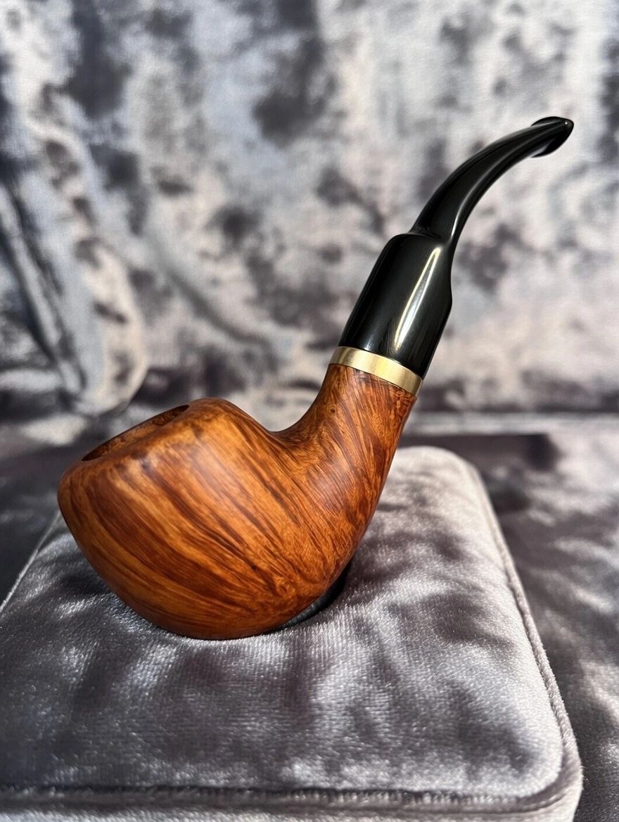 A polished wooden smoking pipe with a black mouthpiece on a soft grey cushion.