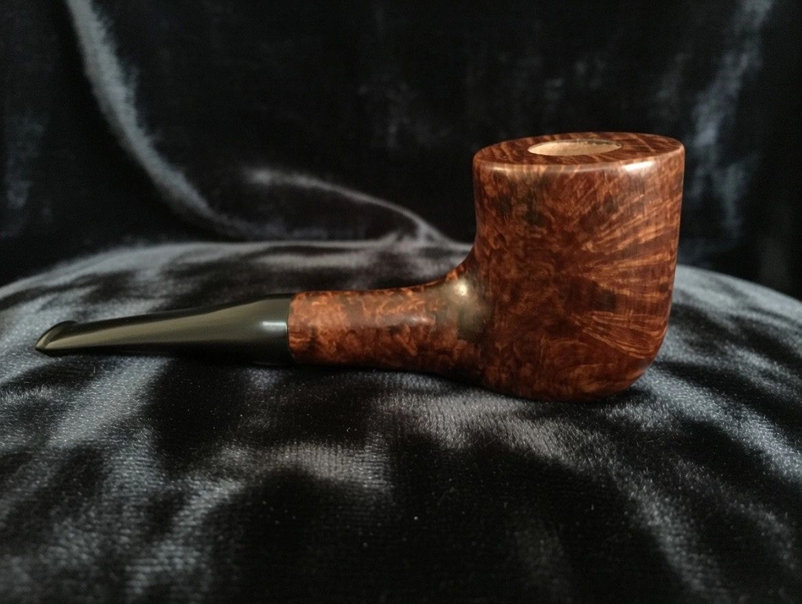 A polished wooden smoking pipe with a black stem on a dark fabric.