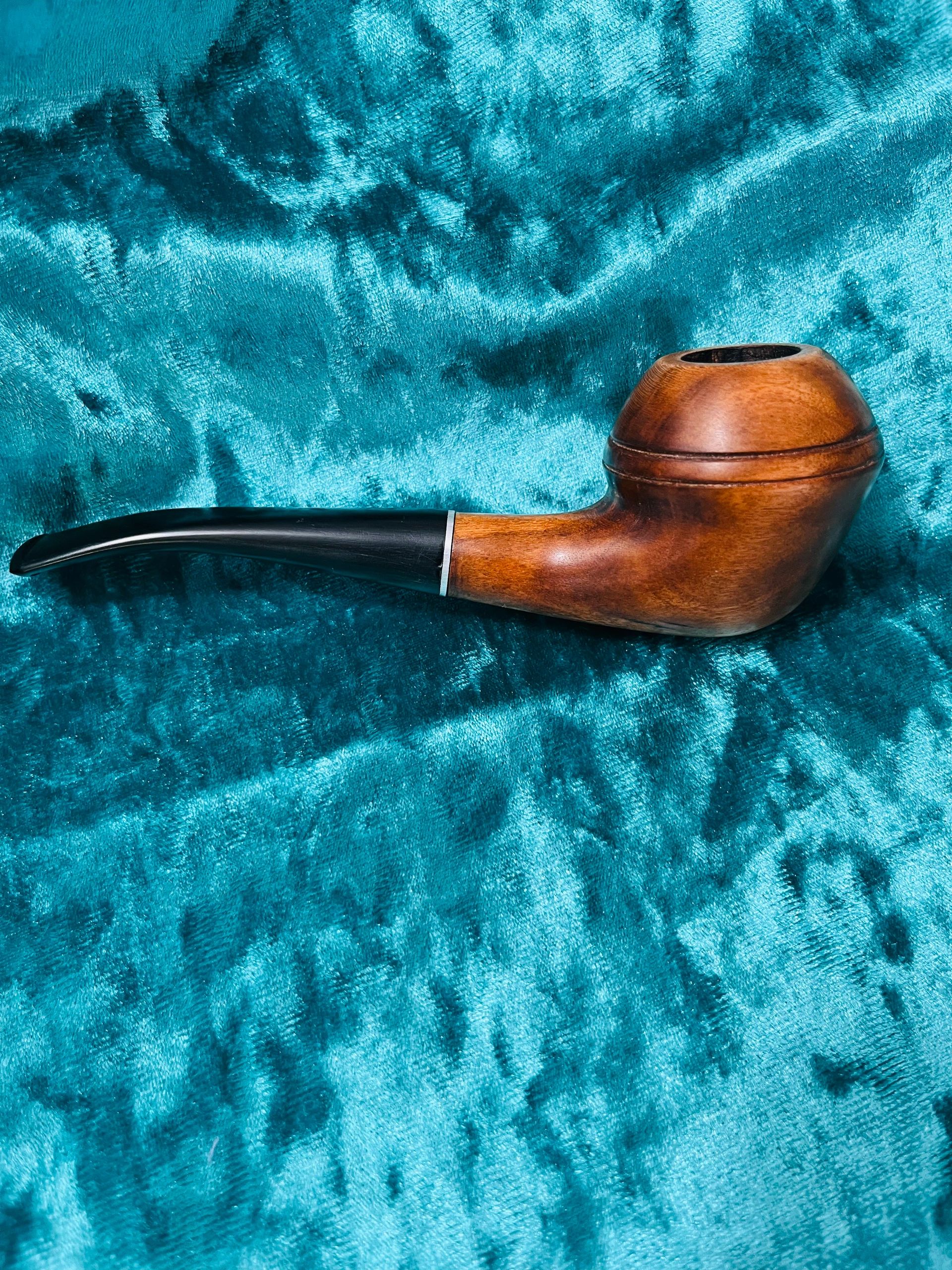 Classic wooden smoking pipe on a textured teal fabric.