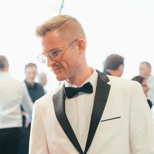 Man in white tuxedo with black bow tie and glasses.
