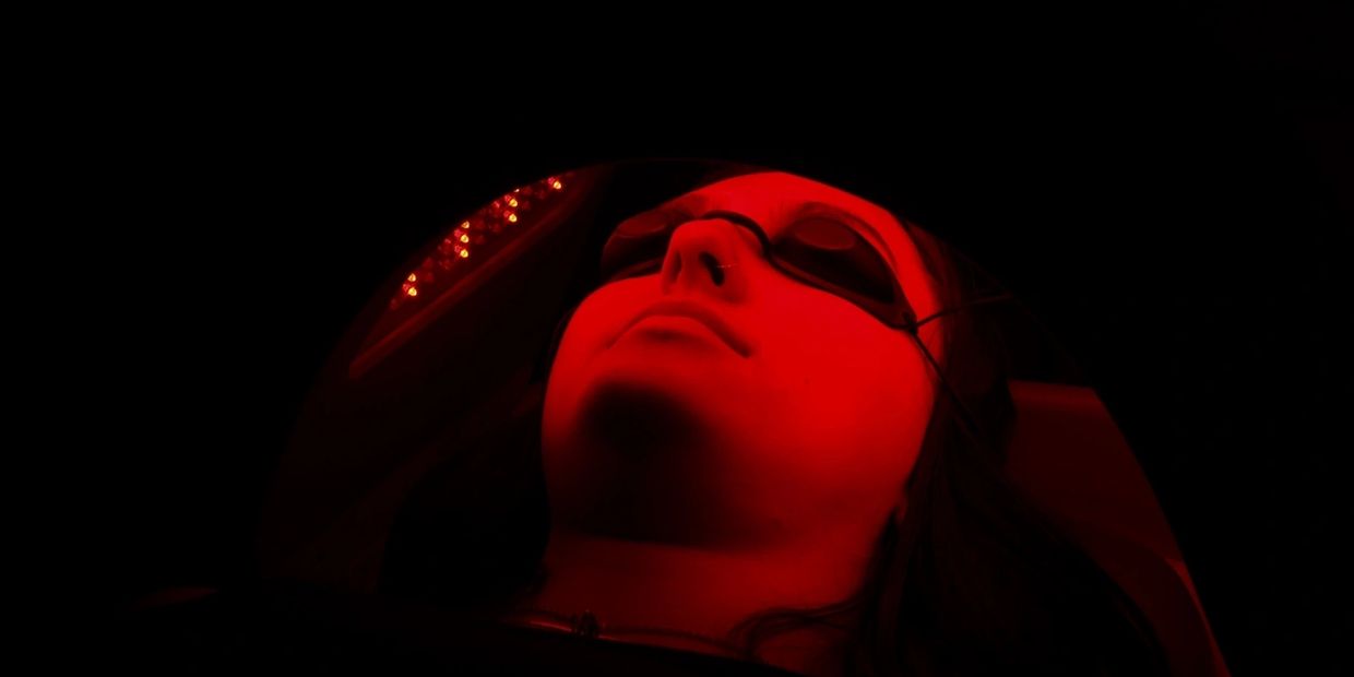 A girl laying underneath a red light therapy device 