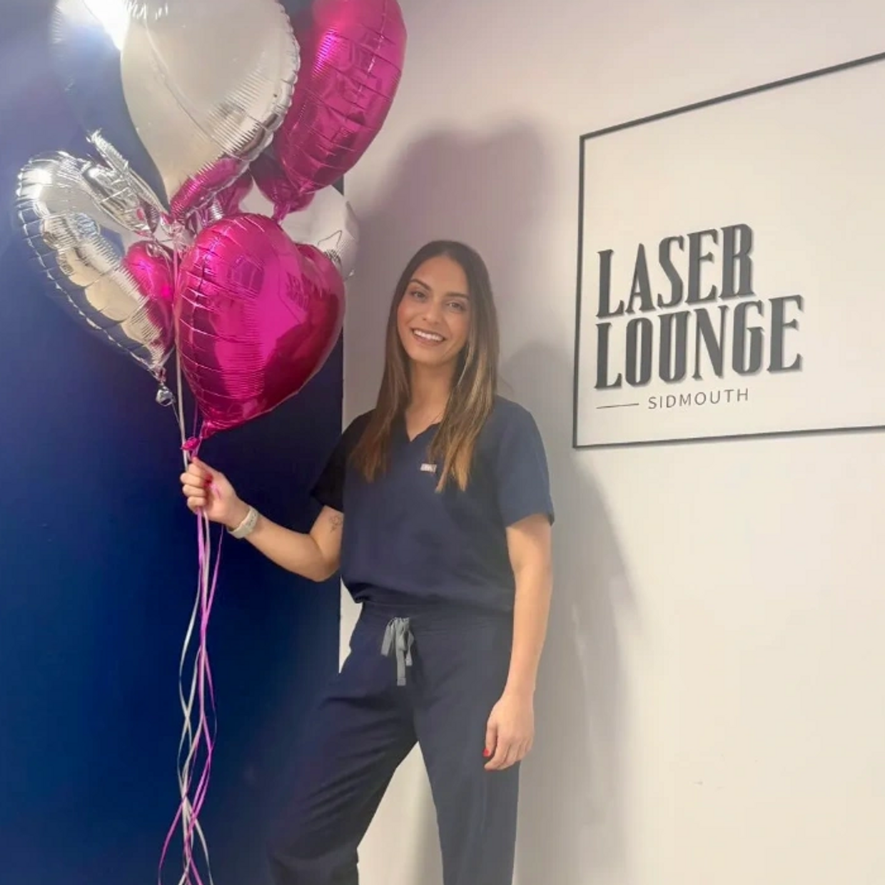A lady holding balloons and wearing navy blue scrubs