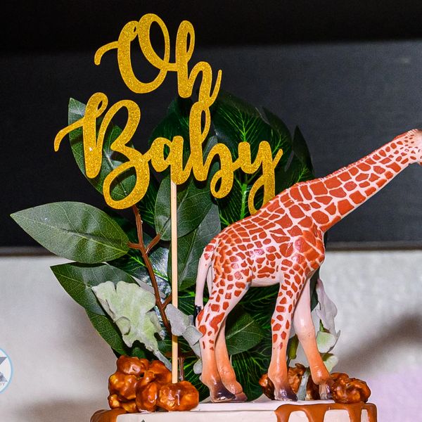 A giraffe cake topper with 'Oh Baby' sign and green leaves.