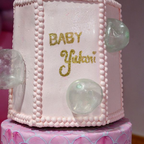 A pink baby shower cake with golden text and decorative bubbles.