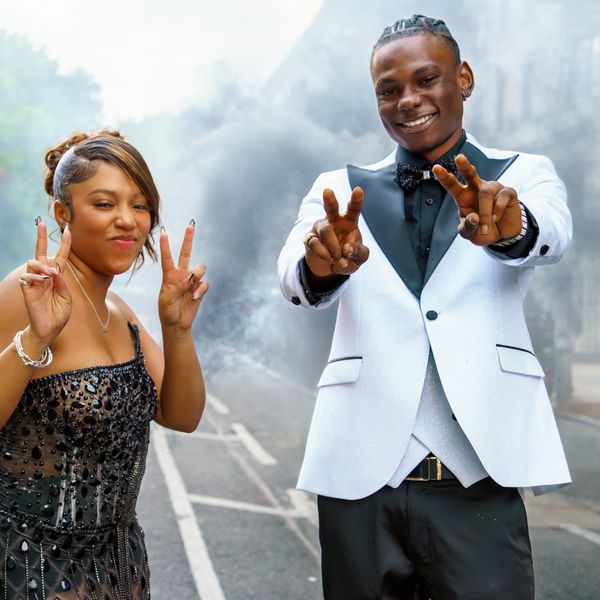 Two young people smiling and posing with peace signs outdoors.