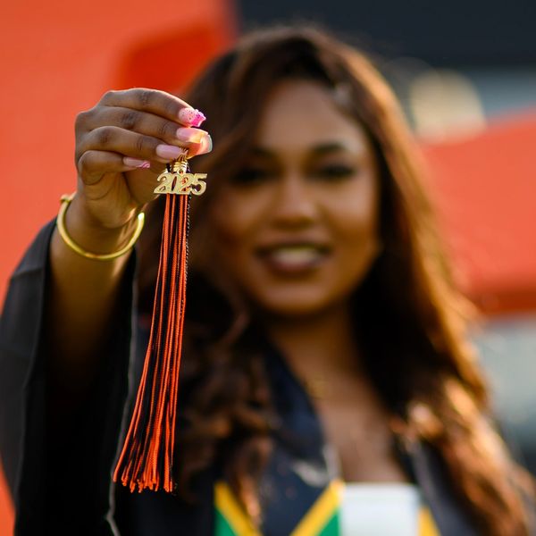 Graduate proudly holds up tassel with the year 2023.