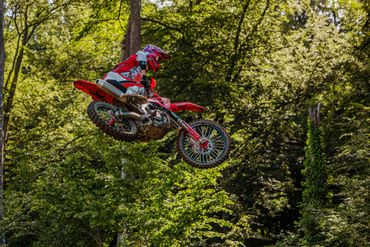 Motorcyclist performing a mid-air jump in a forested area.