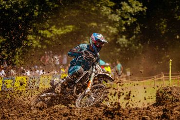 Motocross rider speeding through a muddy track kicking up dirt.