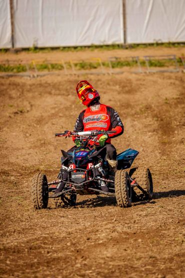 Pilote en tenue rouge sur un quad tout-terrain dans un champ.