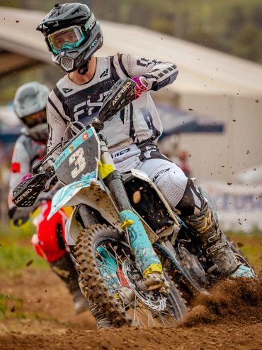 Un pilote de motocross en pleine course sur terrain boueux.
