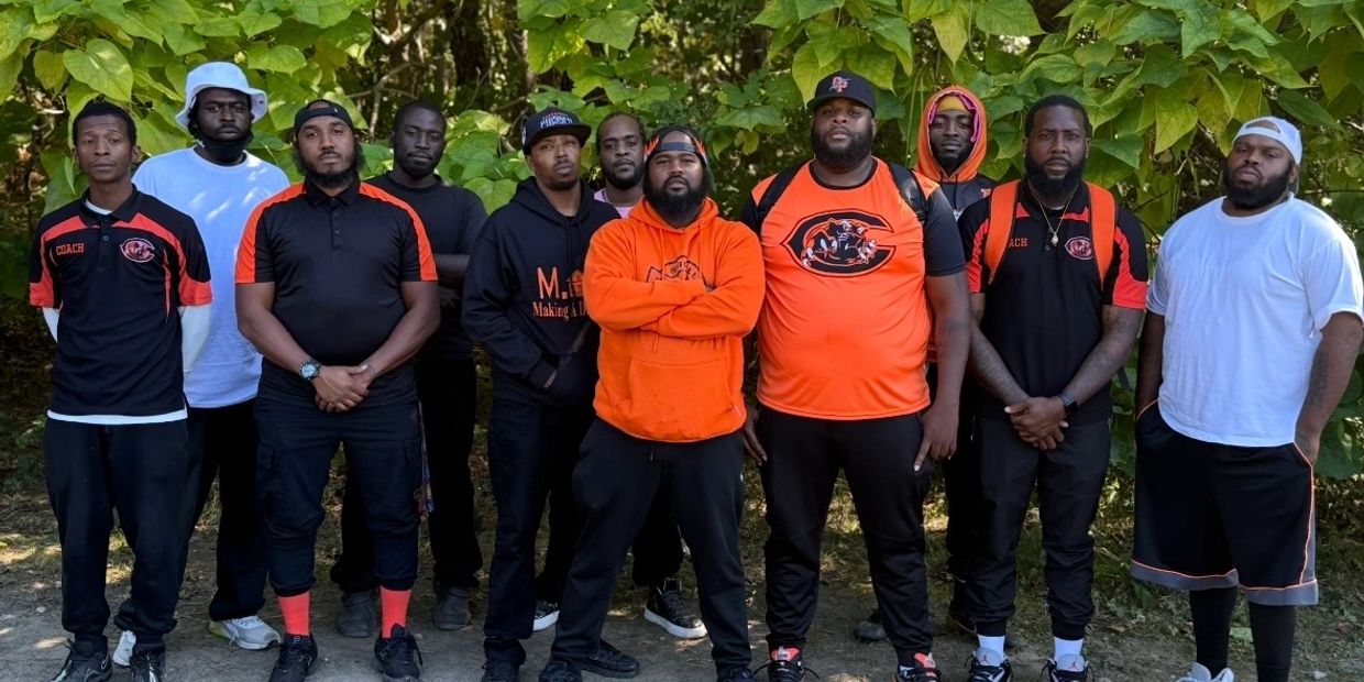 A group of men posing outdoors, some wearing matching black and orange sports attire.