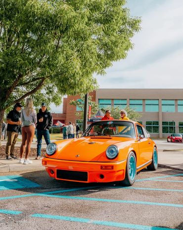 Bright orange vintage Porsche with teal wheels at a car meet.