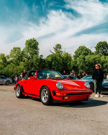 A vibrant red classic Porsche convertible parked outdoors with people around.