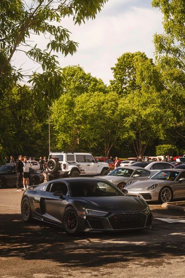 A black sports car parked among other cars in a sunny, tree-lined area.