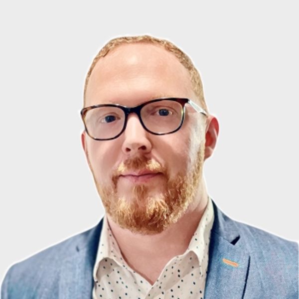 Man with glasses and red beard wearing blazer and collared shirt.