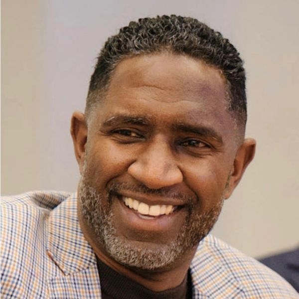 Smiling man with short curly hair and a checked jacket.
