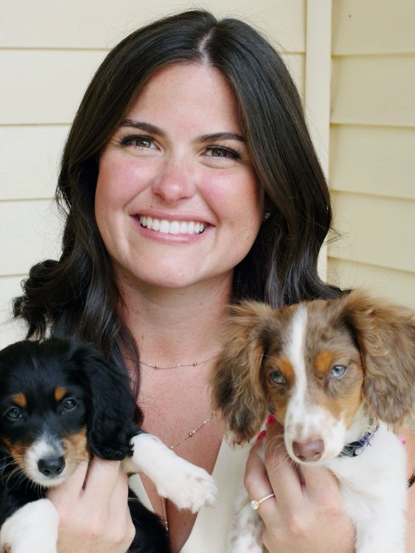 Smiling woman holding two puppies.