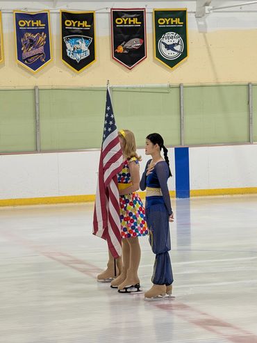 Two figure skaters stand on ice rink holding an American flag.