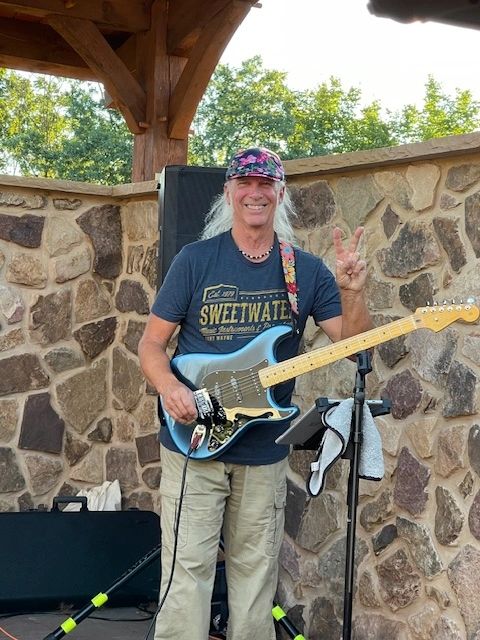 Man smiling with electric guitar and peace sign.