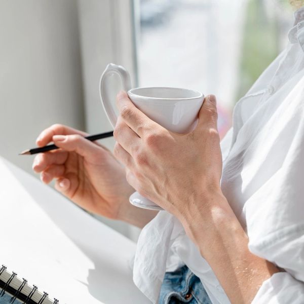 Woman relaxed with a cup of tea and holding a pencil ready to journal