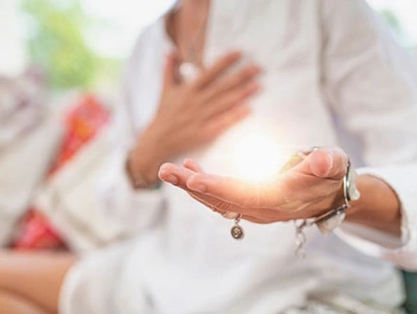 Practitioner with hand on heart and hand held out sending positive reiki healing.