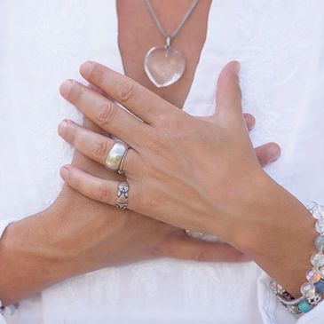 Close up of hands positioned over heart with crystal heart necklace prominently displayed