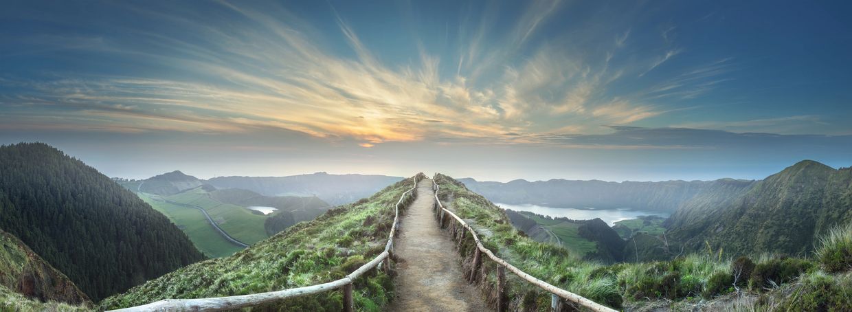 A panoramic mountain top view looking straight down a rustic fenced path trailing off to the sky 