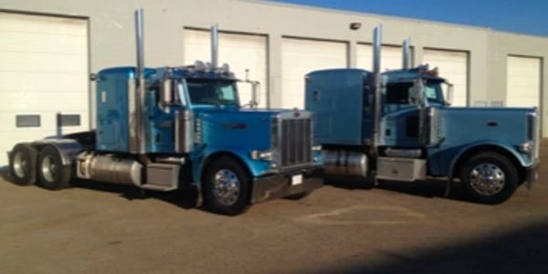Two blue semi-trucks parked outside a building.