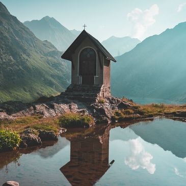Small chapel on rocky hill reflecting in calm mountain lake