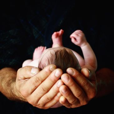 Adult hands gently cradling a newborn baby from above