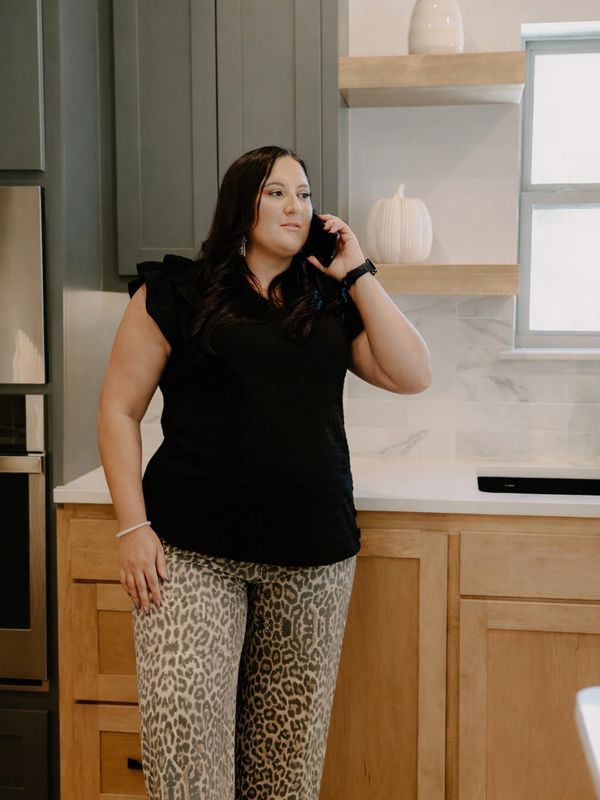 Woman in leopard print pants talking on phone in a modern kitchen.