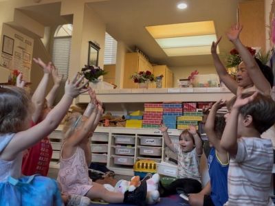 Children and teacher raising hands in a classroom circle.