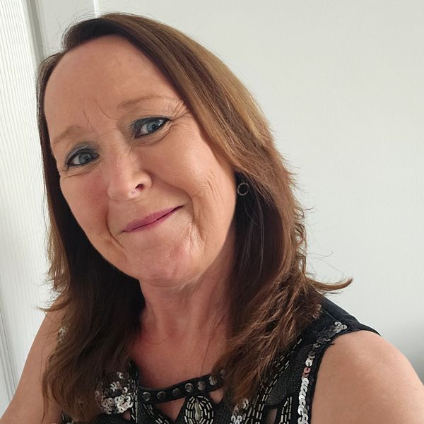 Smiling woman with blue eyes and brown hair wearing a black sequined top.