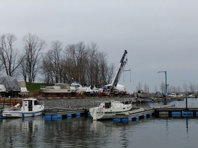 Boats docked at a marina with a crane and leafless trees in the background.