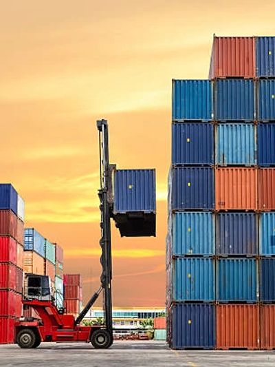 A forklift lifting a blue container at a busy shipping yard during sunset.