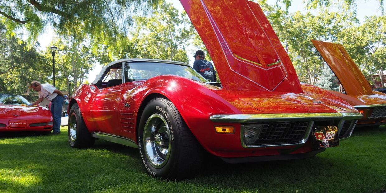 Red classic Corvette with open hood at a car show.