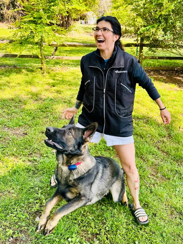 Woman joyfully playing with an attentive German Shepherd dog outdoors.