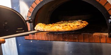 A photo of a pizza coming out of the Toppled Turtle brick oven