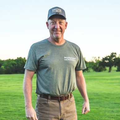Man standing outdoors wearing a cap and casual clothes.