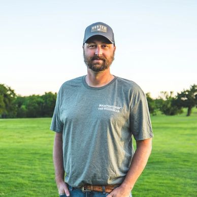 Man standing outdoors on grass wearing a grey shirt and cap.