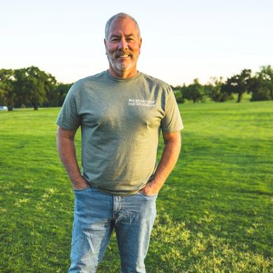 Man standing outdoors with hands in pockets, smiling.