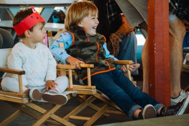 Two children sitting on chairs, one wearing a red paper crown.