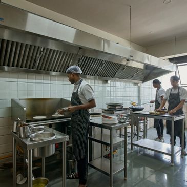 Three chefs preparing food in a clean commercial kitchen with stainless steel equipment.