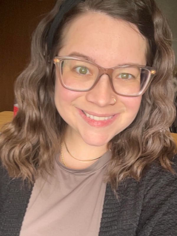 Smiling woman with glasses and wavy hair wearing a black cardigan and beige top.