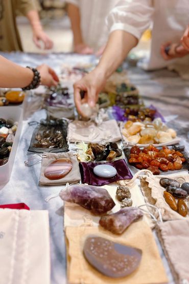Hands selecting polished stones and crystals displayed on a table.
