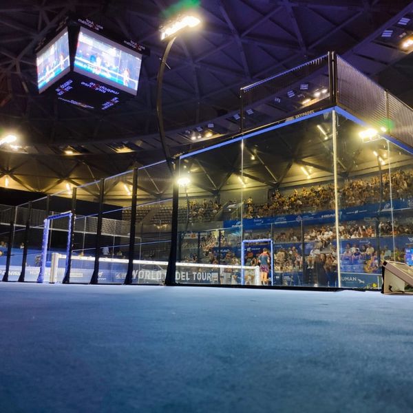 Nighttime padel match in a modern stadium with spectators and illuminated court.