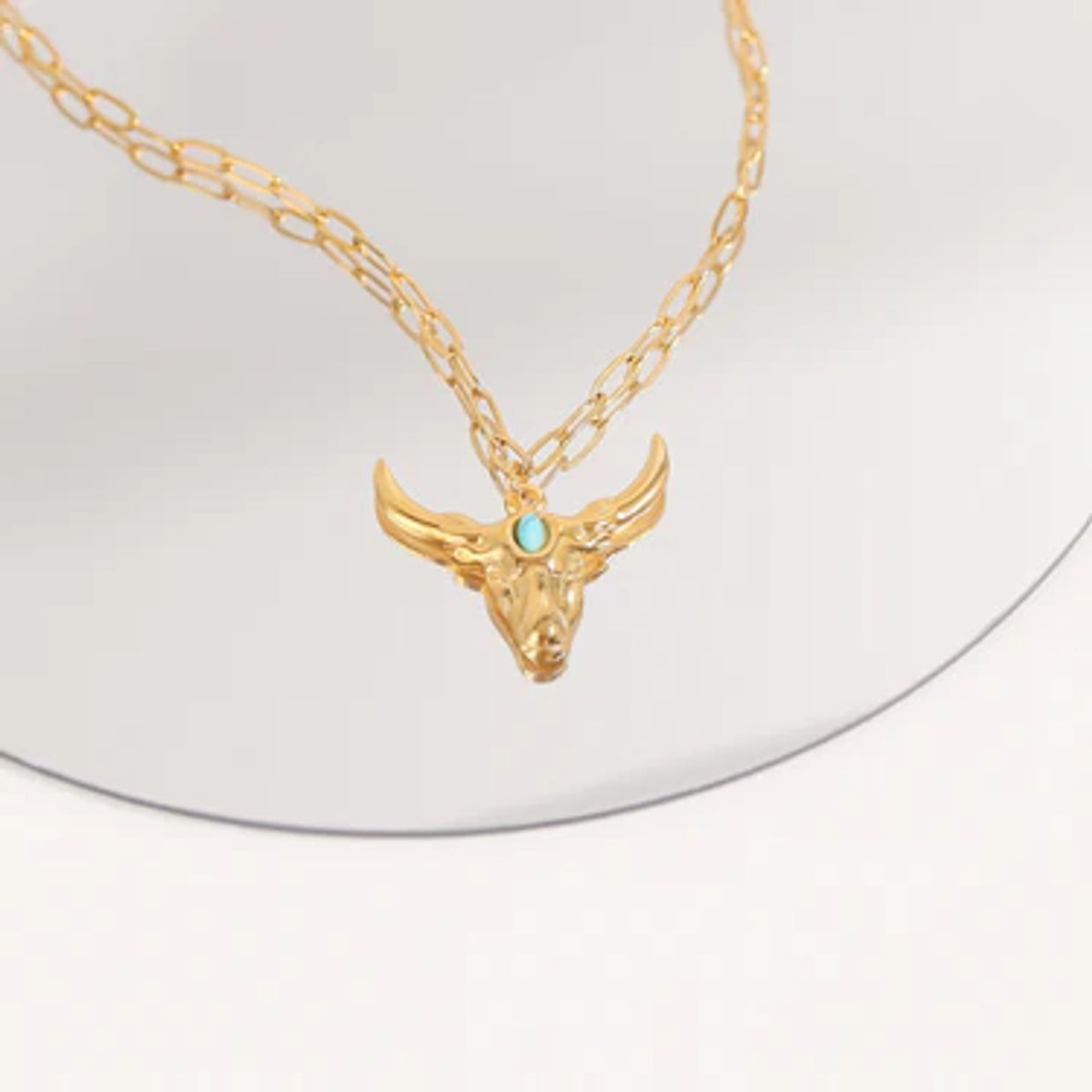 Gold necklace with a bull head pendant and turquoise stone.